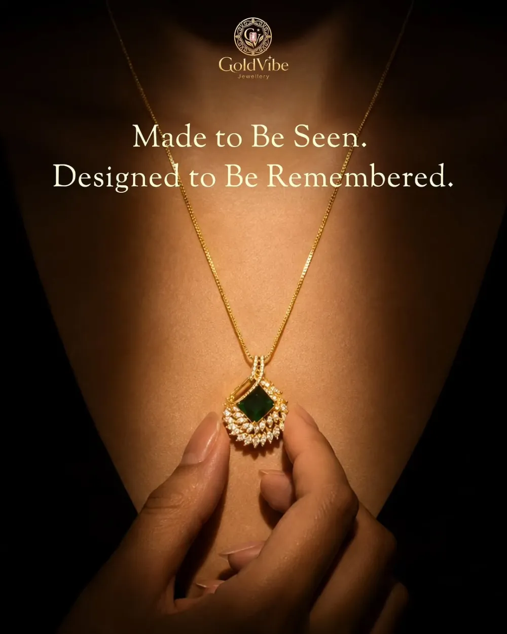 A hand holding an emerald-green square stone pendant on a fine gold chain, lit against a dark ground.